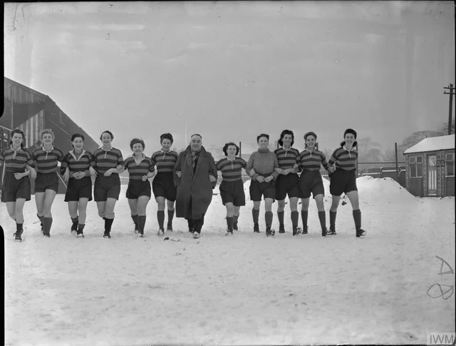 Fotografia de 1944 com o time feminino da fábrica Fairey perfilado ao lado do treinador num campo coberto de neve, depois da vitória por 6 a 0