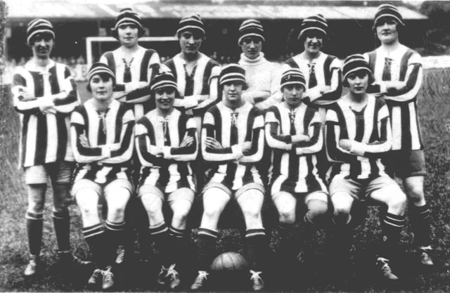 Fotografia do time do Dick, Kerr Ladies perfilado, com bola no chão e o escudo do clube na camisa