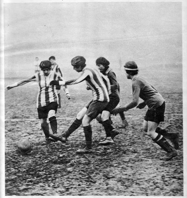 Fotografia dos anos 1920 com jogadoras de camisa listrada e lisa disputando a bola num campo de barro