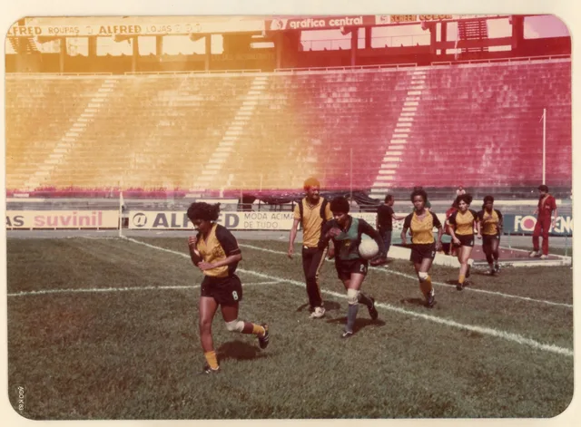 Fotografia colorida de 1983 com jogadoras do Esporte Clube Ypiranga entrando em campo na Fonte Nova, uma delas com a bola