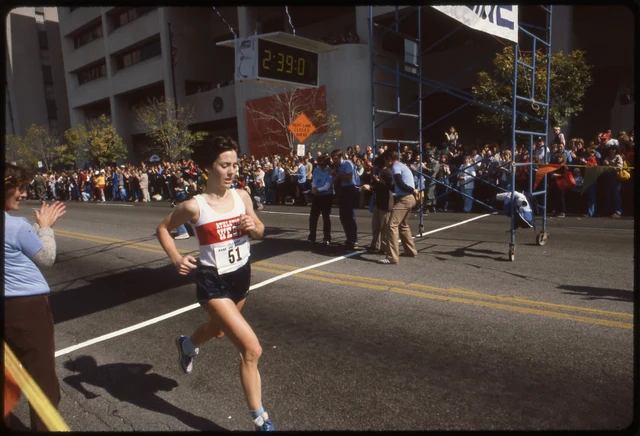 Joan Benoit cruzando a linha de chegada de uma maratona em 1981, de regata e short de corrida